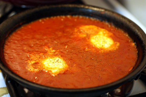 Eggs poaching in tomato sauce in a small iron skillet