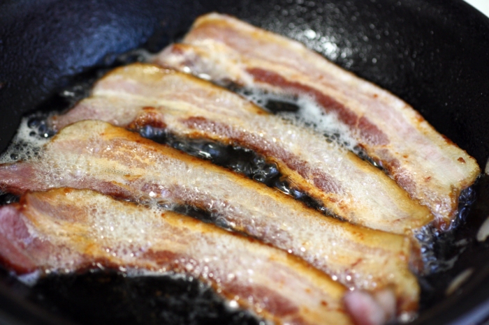 Four strips of bacon sizzling in a cast iron pan